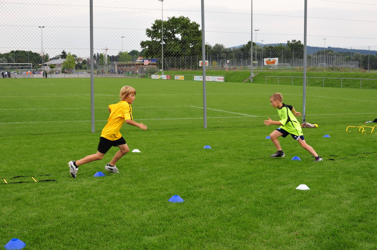 Zwei junge Sportler üben auf dem Rasen Antritt und Richtungswechsel zwischen Markierungshütchen.