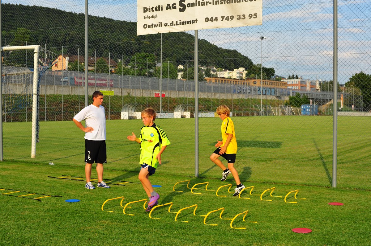 Sascha Göbl begleitet zwei junge Sportler beim Lauf- und Koordinationstraining mit Hürden auf dem Rasen.